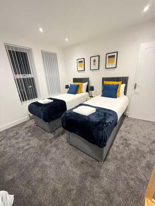 Twin bedroom with navy bedding, yellow accents, grey carpet and vertical blinds