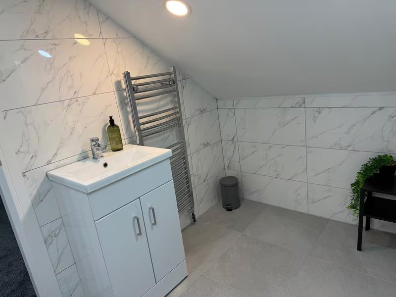 Modern bathroom with marble tile walls, white vanity sink, heated towel rail and recessed lighting