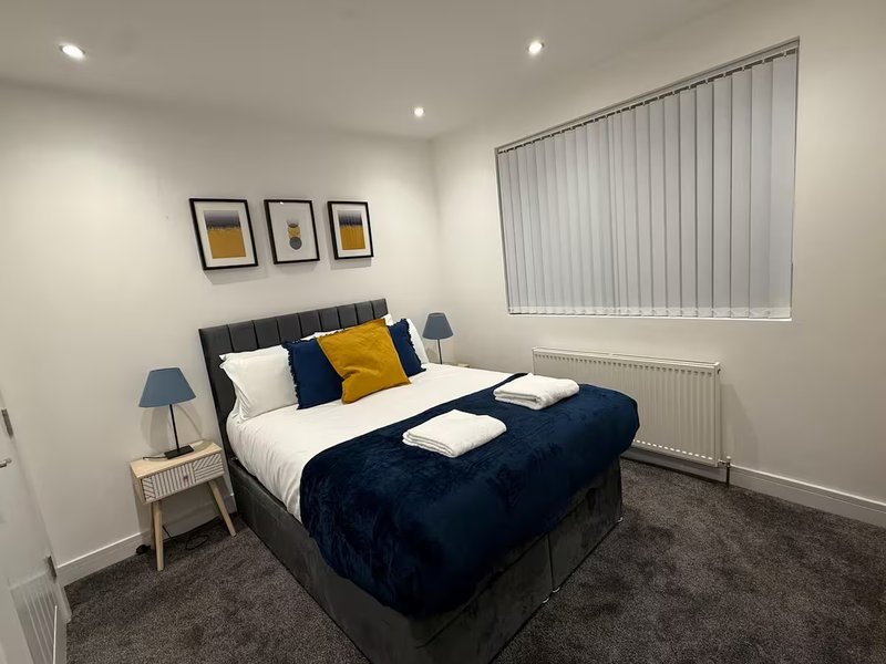 Modern bedroom with double bed, navy bedding, yellow and blue cushions, bedside lamp and framed wall art