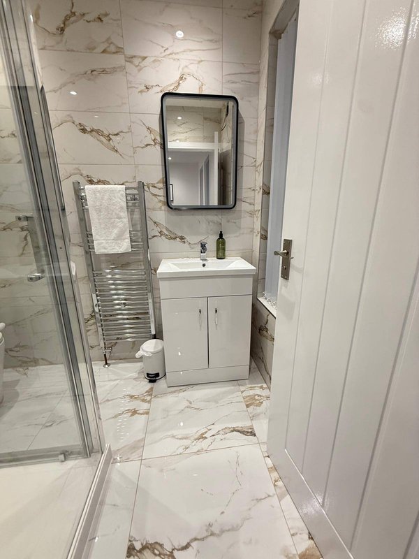 Modern bathroom with marble-effect tiles, white vanity, black-framed mirror and towel rail