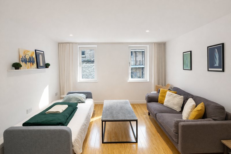 Bright modern living room with grey sofa, single bed, coffee table and wooden flooring