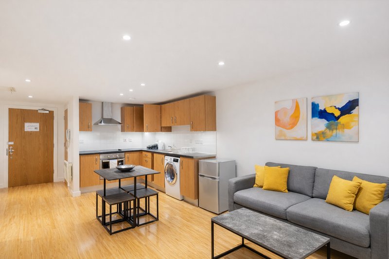 Open-plan living area with wooden kitchen, dining table, gray sofa and yellow cushions