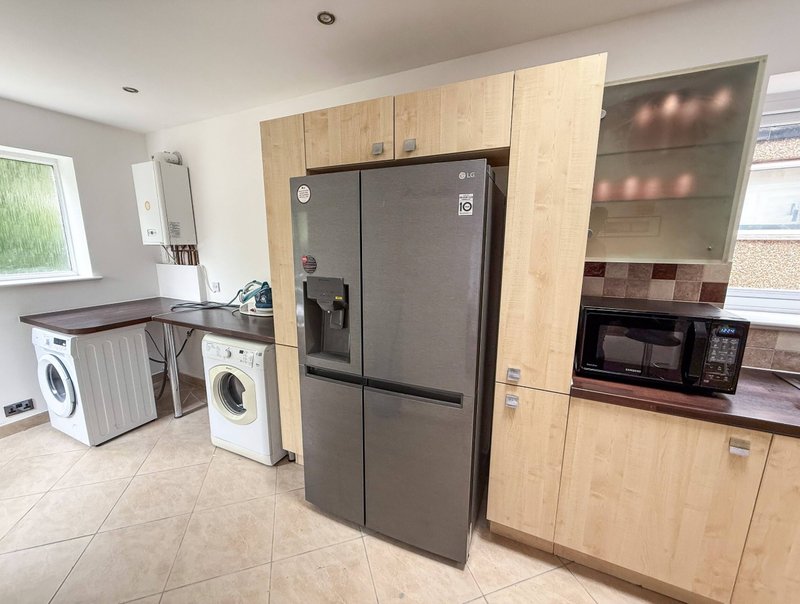 Modern kitchen with black fridge, wooden cabinets, washing machines and microwave