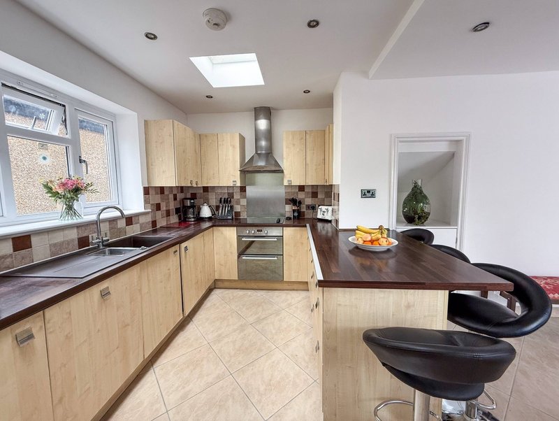 Modern kitchen with light wood cabinetry, black countertops, stainless steel appliances and island seating