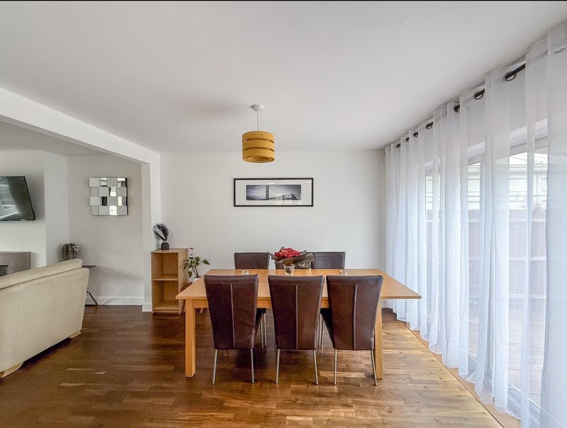 Open-plan dining and living area with wooden table, leather chairs and pendant light