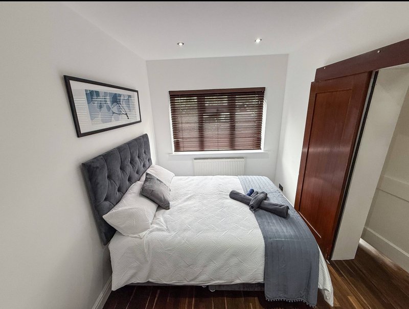 Compact bedroom with double bed, grey headboard, white bedding and dark wooden wardrobe