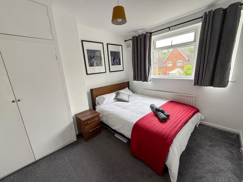 Bedroom with single bed, red throw, wooden headboard, wardrobe and window view