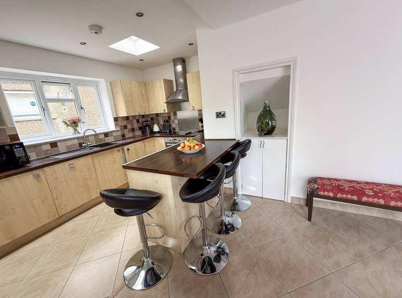Modern kitchen with light wood cabinets, black countertop, island with bar seating, and adjoining dining area