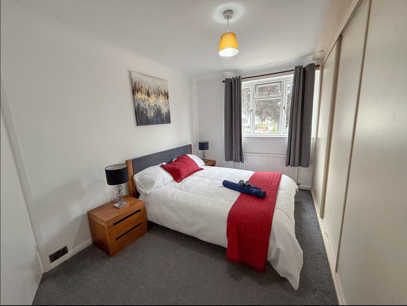 Bedroom with double bed, wooden nightstand, pendant lamp, and window with grey curtains