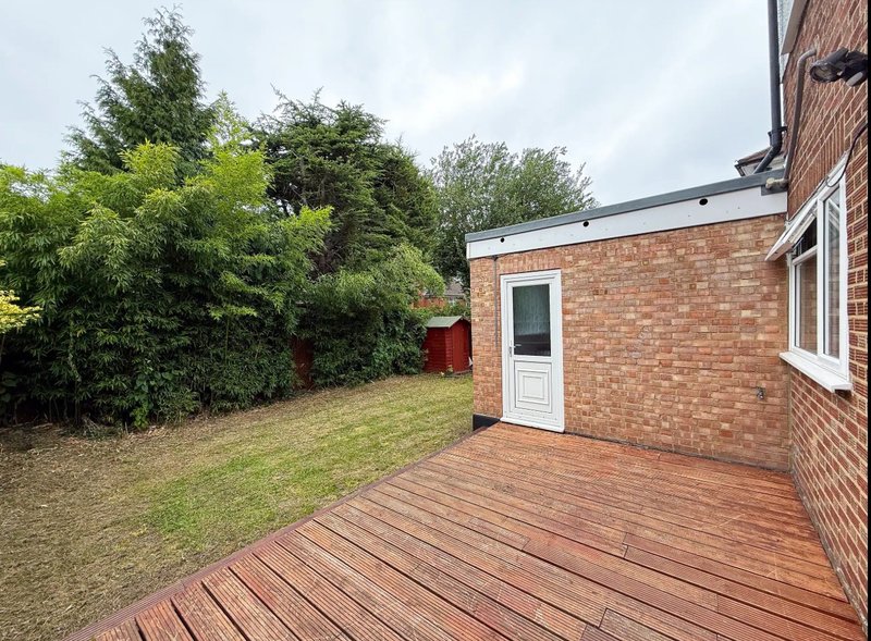 Brick house exterior with wooden deck, garden, and mature trees
