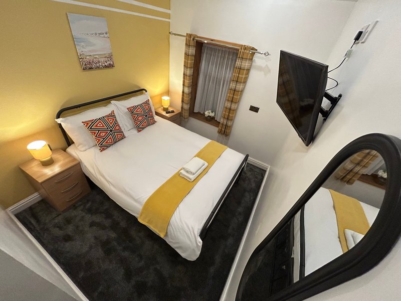 Modern bedroom with double bed, yellow accents, bedside lamps, wall-mounted TV and mirror