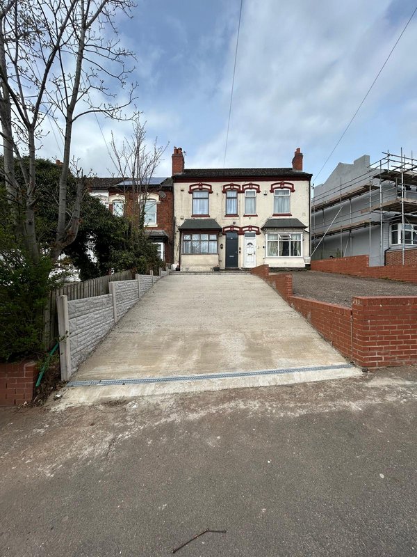 Brick house with driveway, front garden, and neighboring scaffolding visible