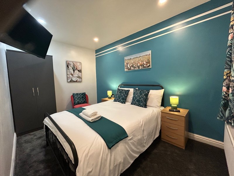 Modern bedroom with teal accent wall, double bed, wooden nightstands and yellow lamps