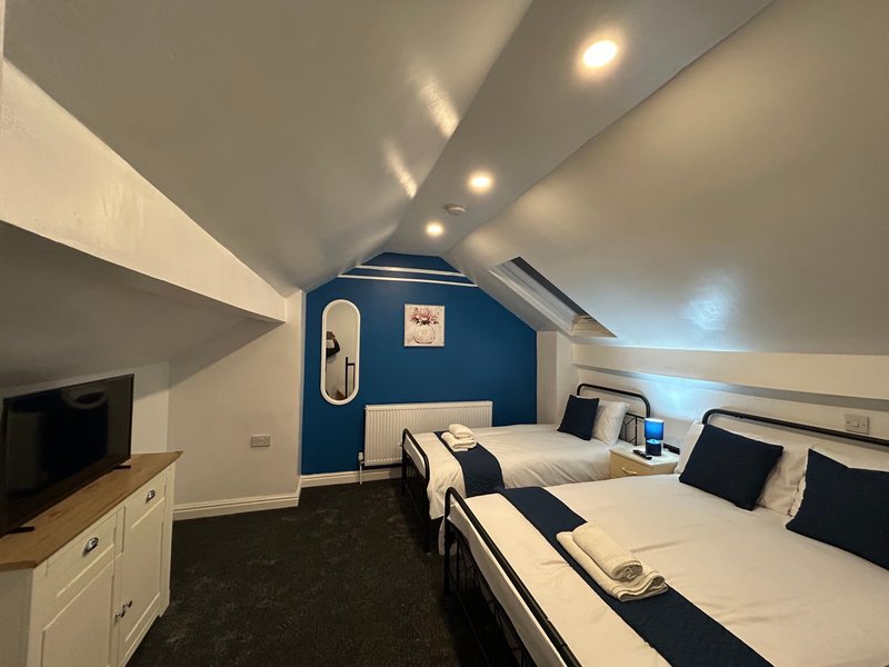 Attic bedroom with two beds, dark carpet, blue feature wall and recessed lighting