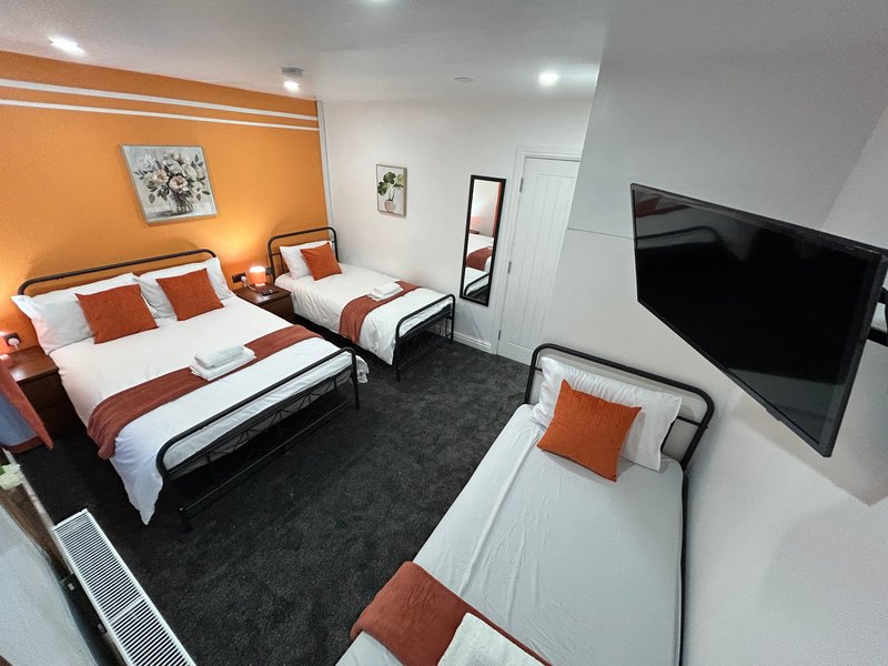Modern bedroom with three beds, orange and white bedding, TV, and orange accent wall