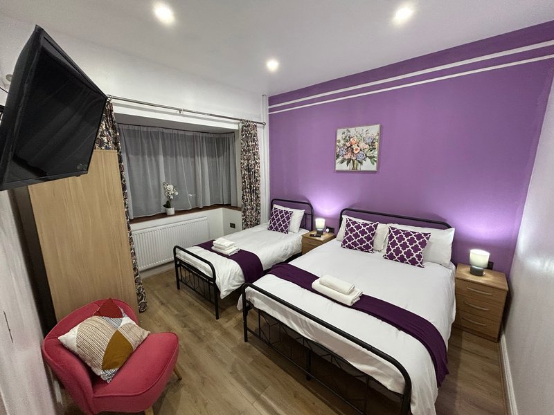 Bright bedroom with two single beds, purple accent wall, pink armchair and mounted TV