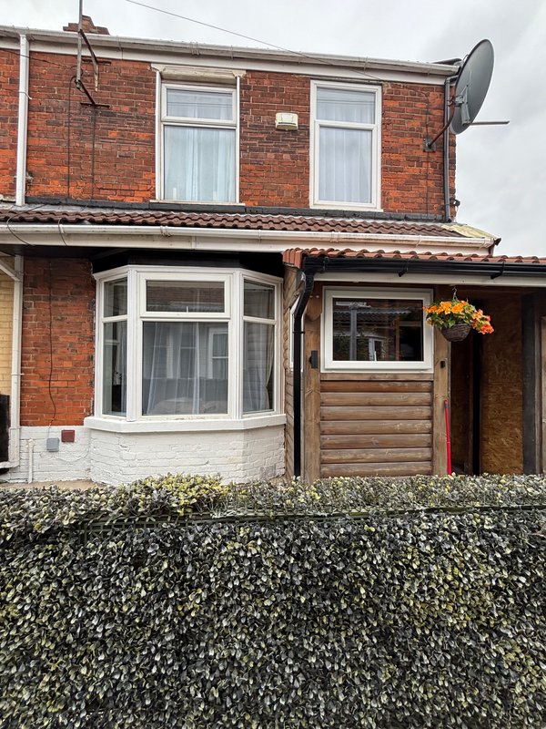 Red brick terraced house with bay window, wooden cladding, and front hedge