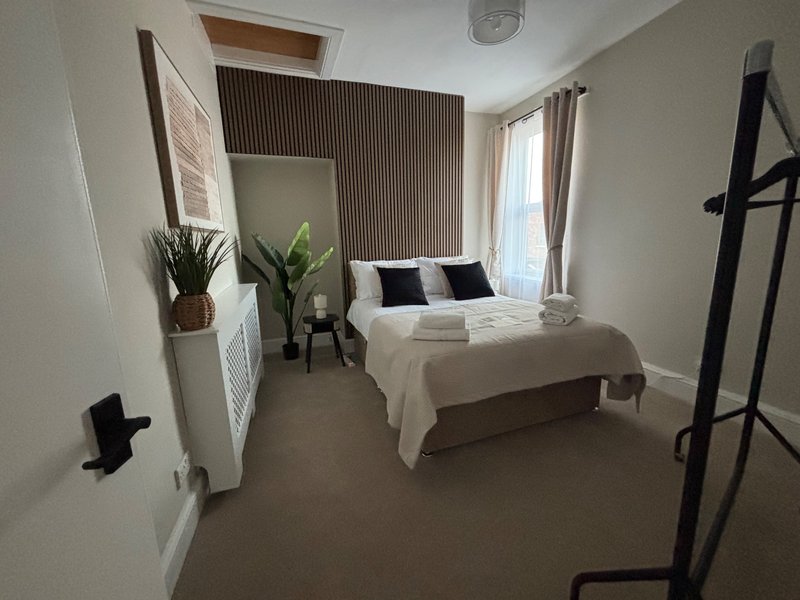 Modern bedroom with double bed, potted plants, mirror, and natural light from windows
