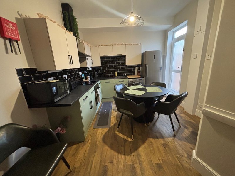 Modern kitchen and dining area with black subway tiles, cream cabinets, wooden flooring and dining table