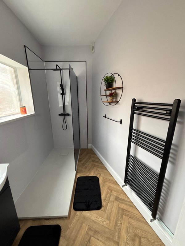 Modern bathroom with walk-in shower, black heated towel rail, herringbone flooring, and window