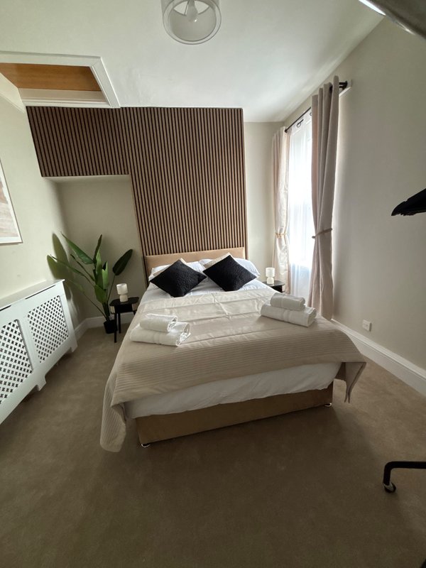 Bright bedroom with double bed, black cushions, wooden accent wall and window with curtains