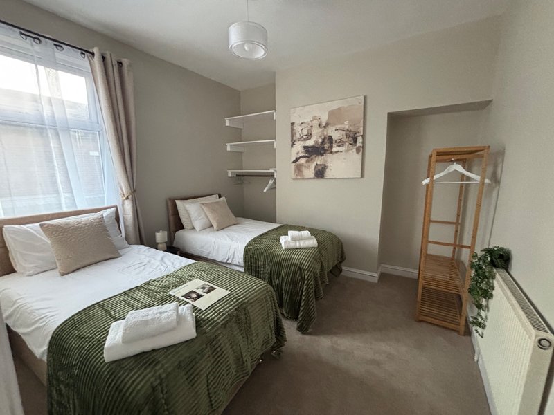 Twin bedroom with two beds, green quilts, white towels, window with curtains