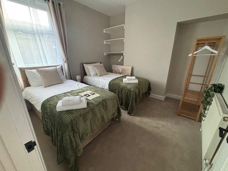 Twin bedroom with two single beds, green throws, wooden mirror and shelving unit