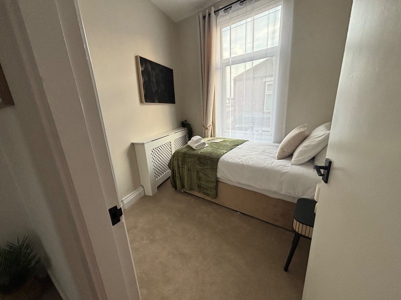 Small bedroom with single bed, window with curtains, radiator and potted plant