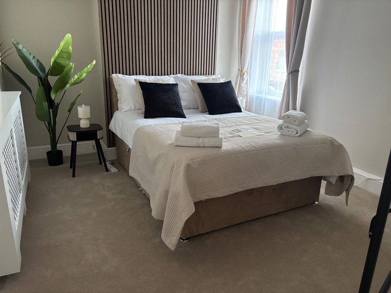 Modern bedroom with double bed, dark headboard, black and white pillows, potted plant, and floor-to-ceiling windows