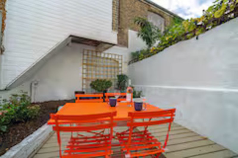 Bright outdoor patio area with orange furniture, wooden decking, and white walls