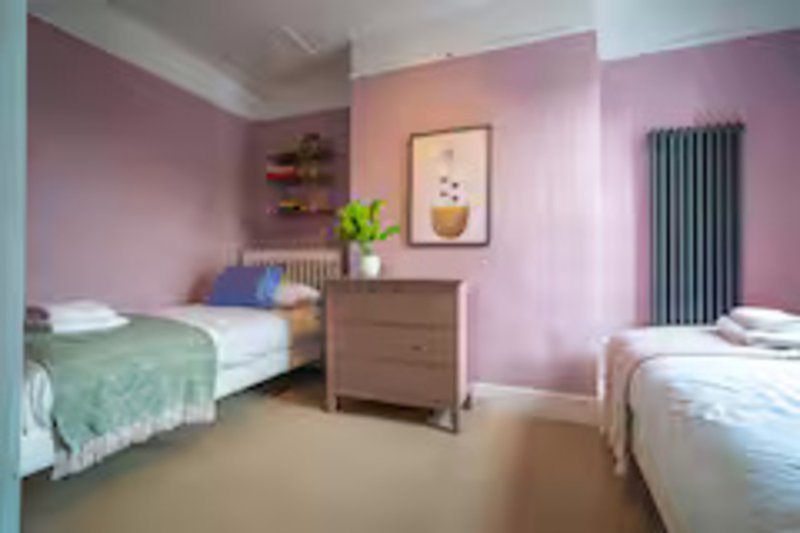 Shared bedroom with two single beds, wooden dresser, pink walls and potted plant