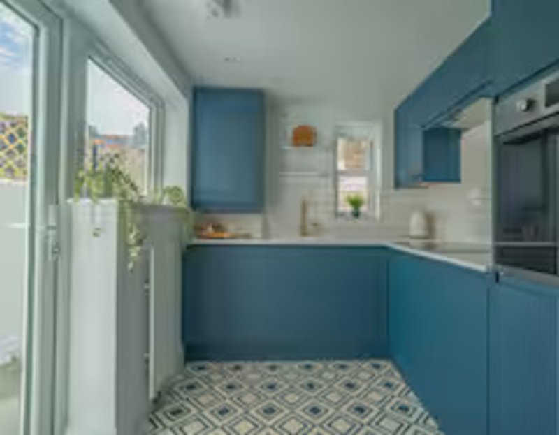 Modern kitchen with teal cabinetry, patterned floor tiles, and patio door to garden