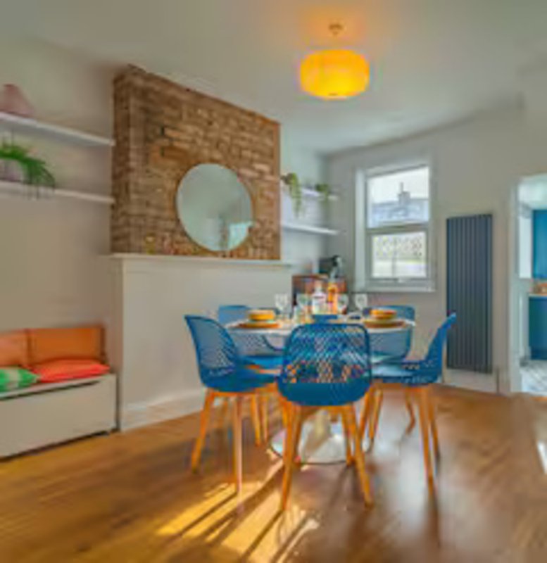 Modern dining area with blue chairs, round table, brick wall feature and yellow ceiling lamp