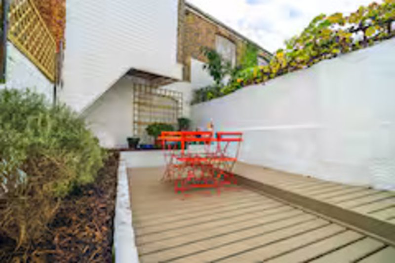 Contemporary courtyard with wooden decking, red chairs, white walls and climbing plants