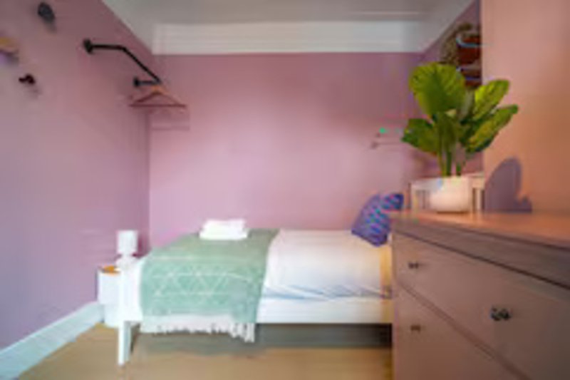 Pink bedroom with single bed, white nightstand, wooden dresser and potted plant