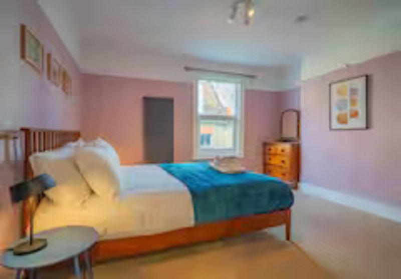 Pink bedroom with wooden bed, blue bedding, wooden dresser and bedside lamp