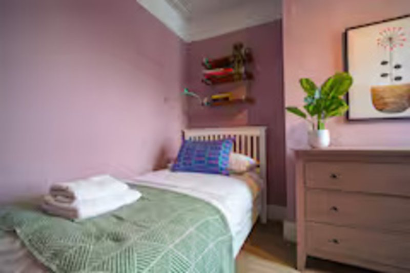 Bedroom with single bed, green bedding, pink walls, wooden dresser and wall art