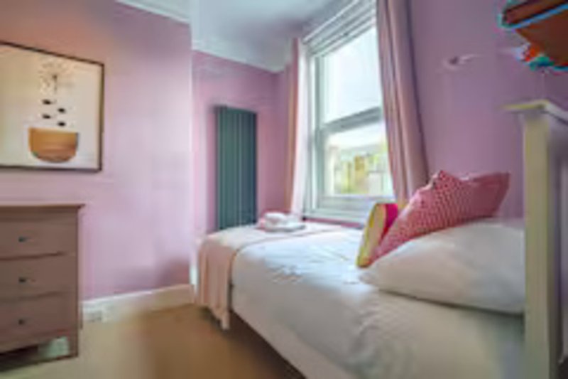 Bright pink bedroom with two single beds, wooden dresser, window and framed wall art