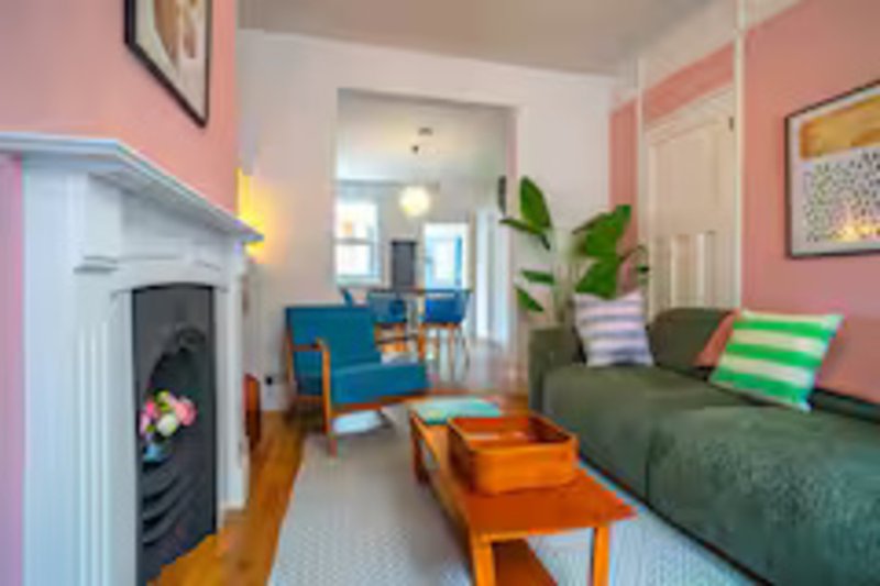 Open-plan living room with fireplace, blue armchair, green sofa, orange coffee table and wooden flooring