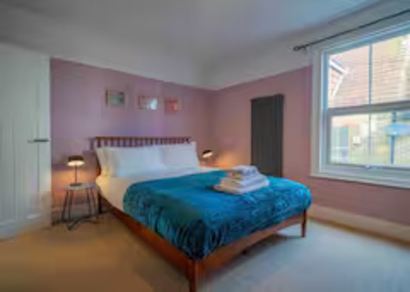 Modern bedroom with blue duvet, wooden bed frame, pink walls and large window