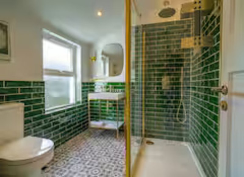 Modern bathroom with green tile walls, walk-in shower, toilet, sink and window