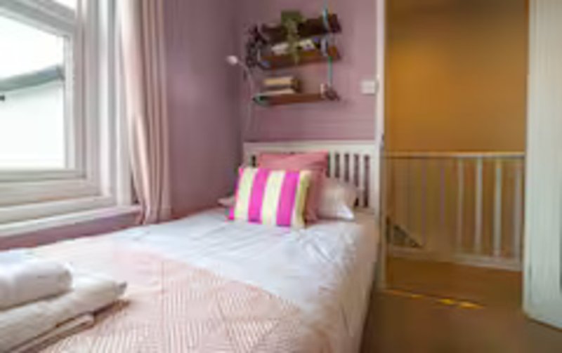 Small bedroom with single bed, pink walls, striped cushion, shelving and window