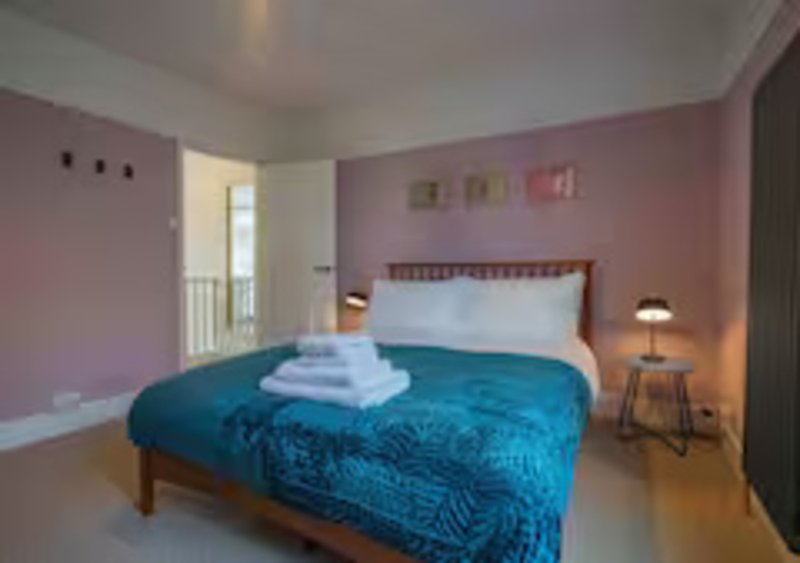 Pink bedroom with double bed, blue bedding, white pillows, bedside lamp and wooden furniture