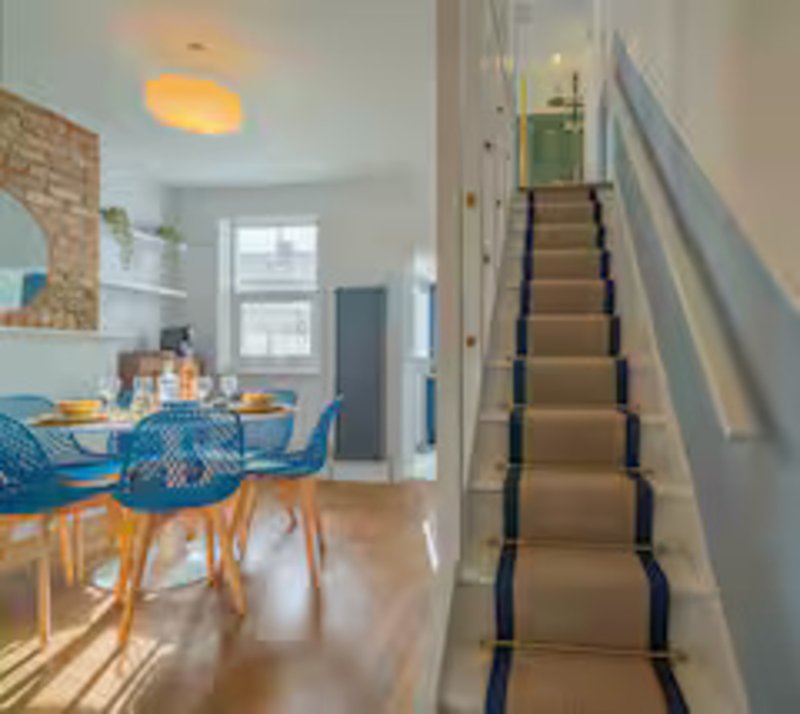 Open-plan kitchen and dining area with blue chairs, wooden floor, and staircase with dark runner