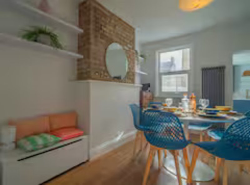 Open-plan living and dining area with orange bench seating, wooden dining table, blue chairs and brick fireplace