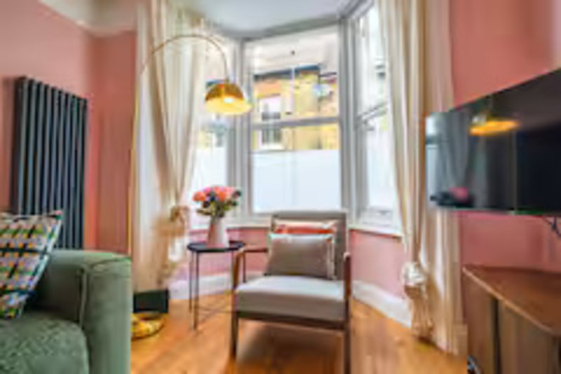 Bright living room with pink walls, green sofa, wooden chair, flowers on table, and TV