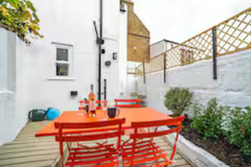 Bright outdoor patio area with red dining table, chairs, potted plants and wooden decking