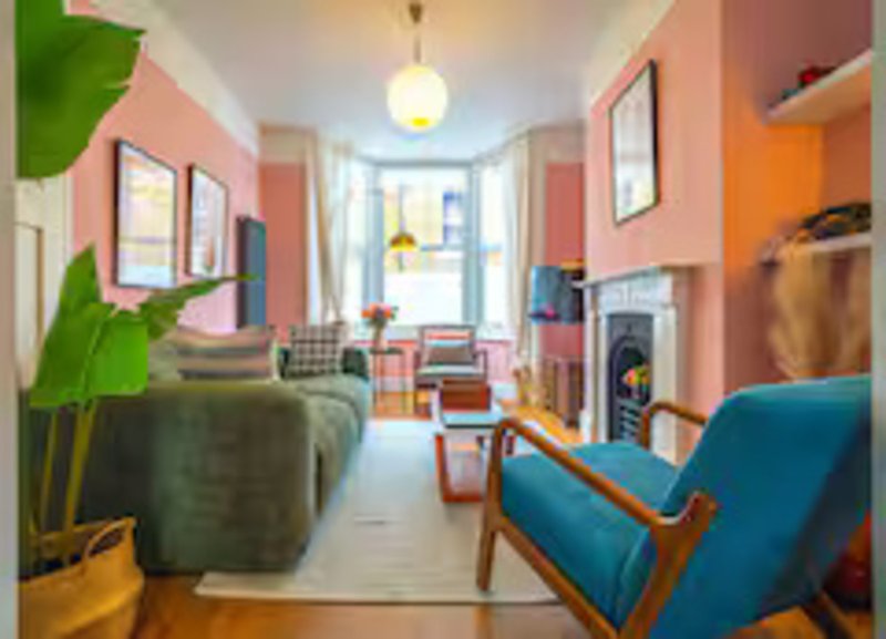 Colorful open-plan living room with pink walls, green sofa, blue armchair, fireplace and front door
