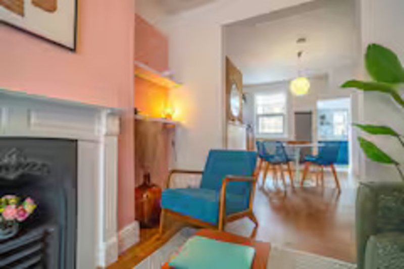 Living room with pink accent wall, fireplace, blue armchairs, and wooden flooring