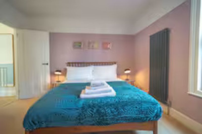 Bedroom with double bed, blue bedding, pink walls, bedside lamps and radiator